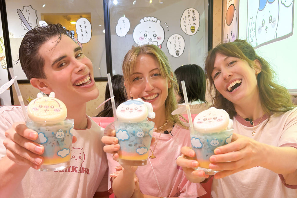 Three people holding colorful Chiikawa drinks with cartoon designs in Chiikawa Cafe in Tokyo.